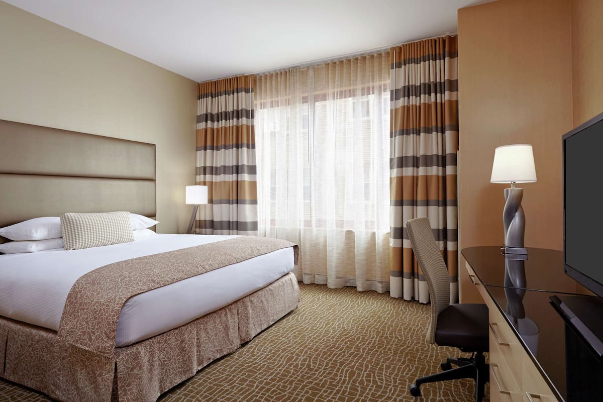 A hotel room with a large bed, a desk with a TV, and a chair.