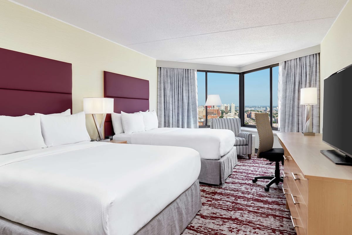 A hotel room with two beds, a desk, a chair, and a TV.