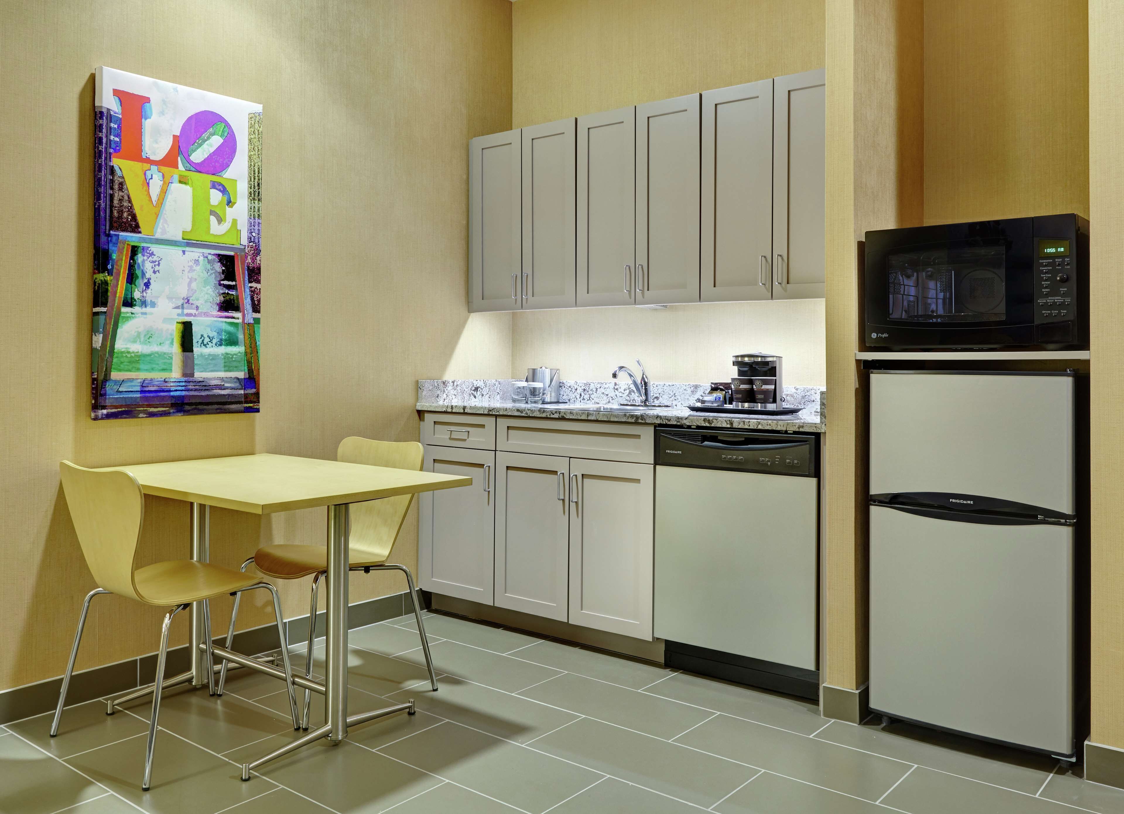 A compact kitchen with a dining area, featuring cabinets, a microwave, a refrigerator, and a coffee maker.
