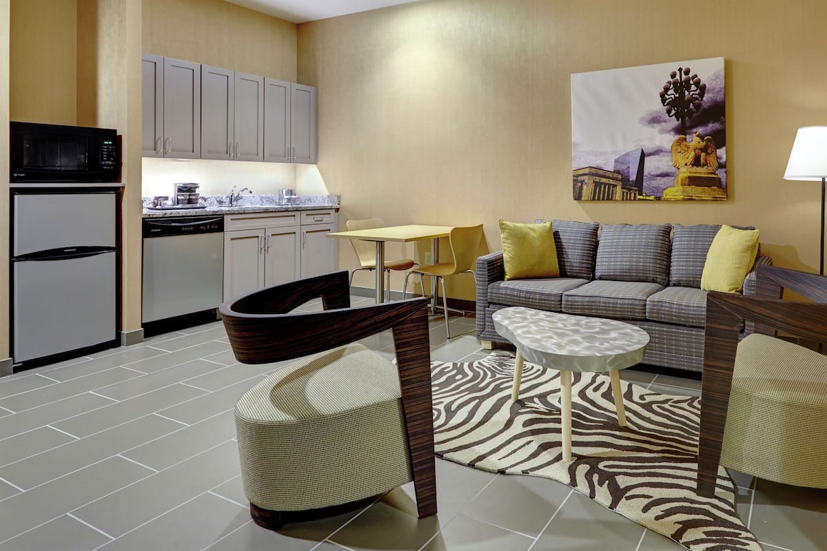 A compact living space with a kitchenette, a sofa set, a dining table, and a zebra-patterned rug.