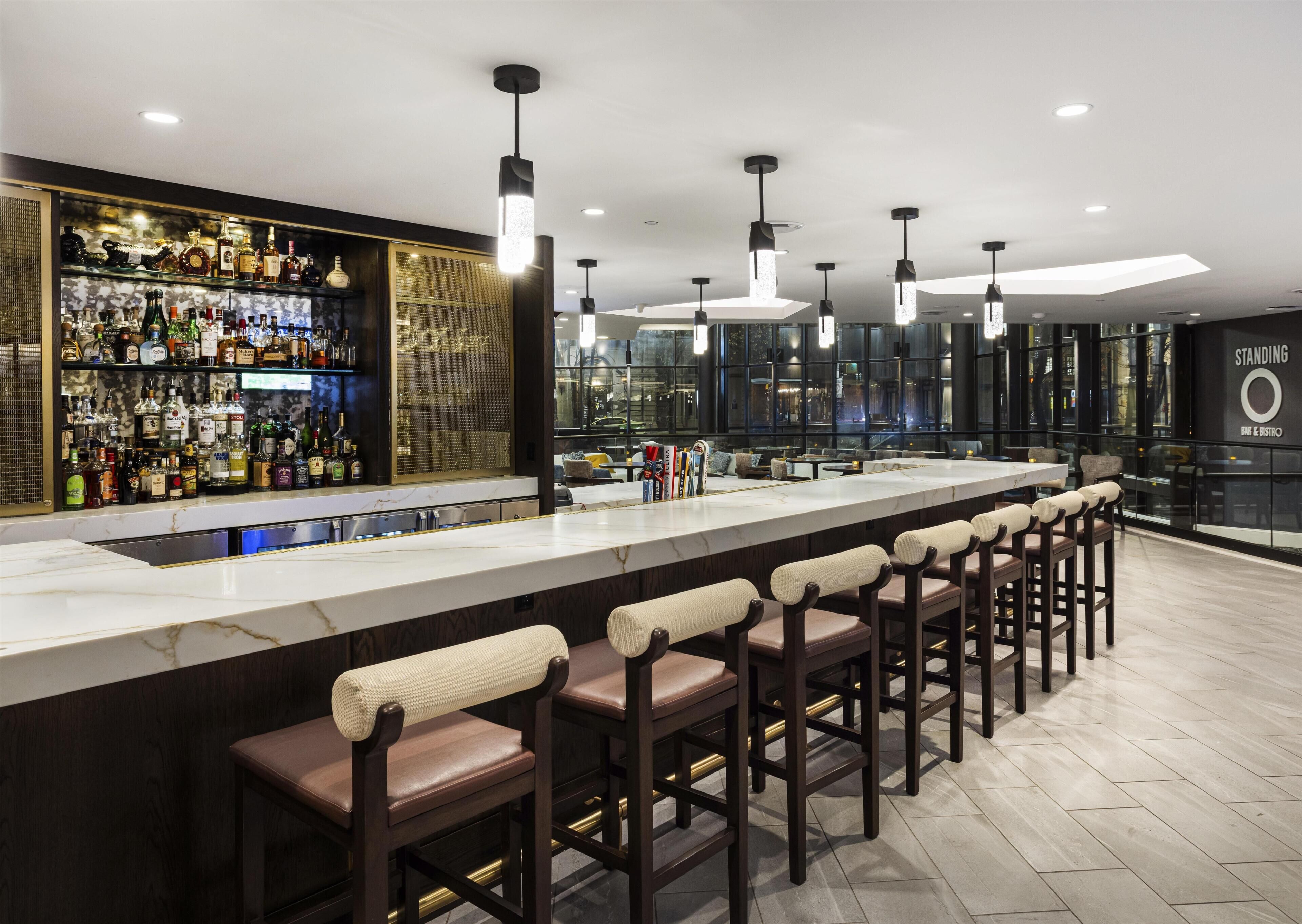 A bar area with a long counter, multiple stools, and a well-stocked liquor shelf.