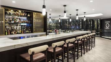 A bar area with a long counter, multiple stools, and a well-stocked liquor shelf.