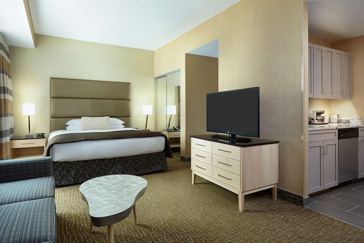A hotel room with a bed, a TV, a sofa, a desk, and a kitchenette.