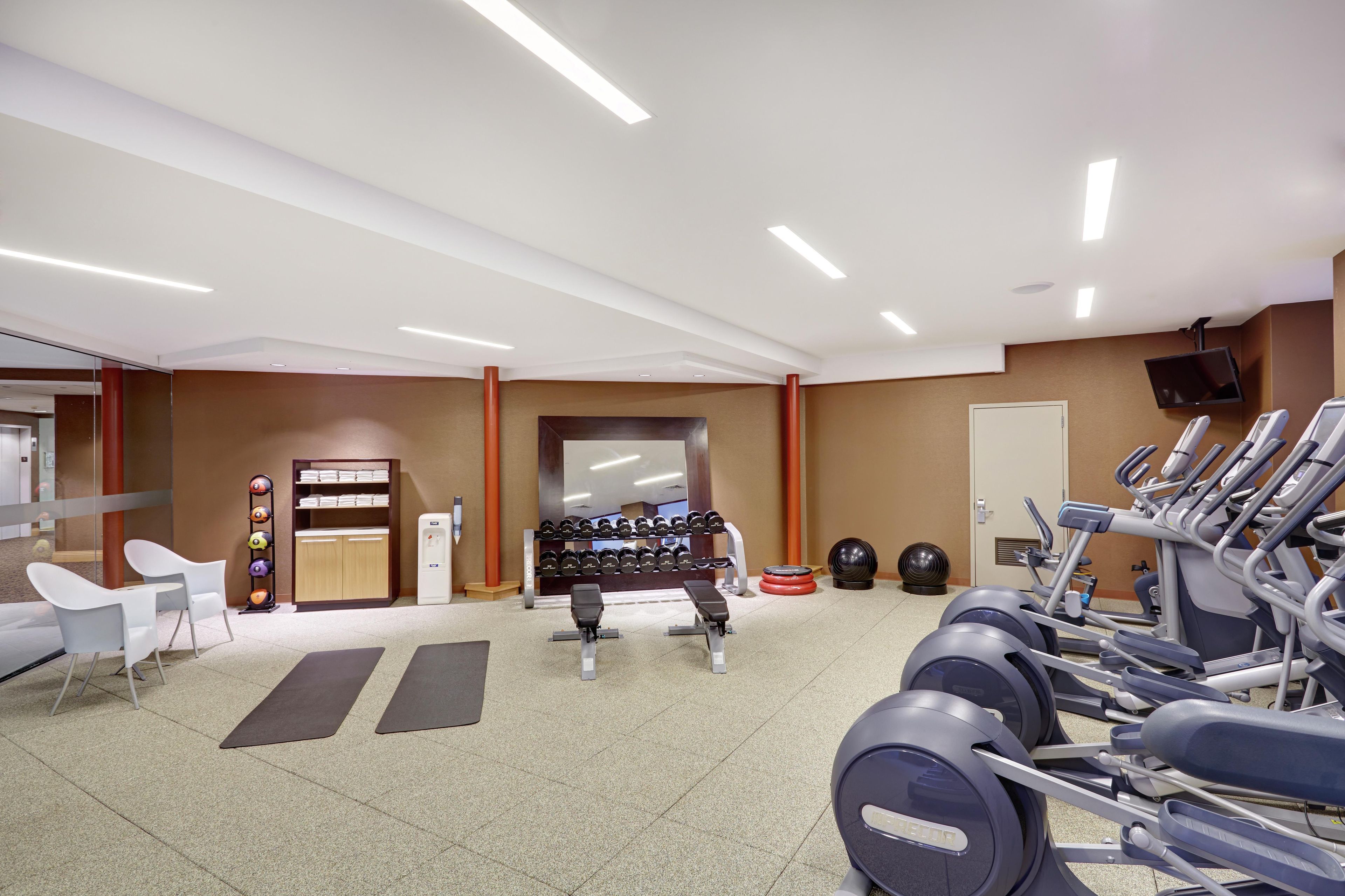A gym with exercise equipment, a bench, dumbbells, and a wall-mounted TV.