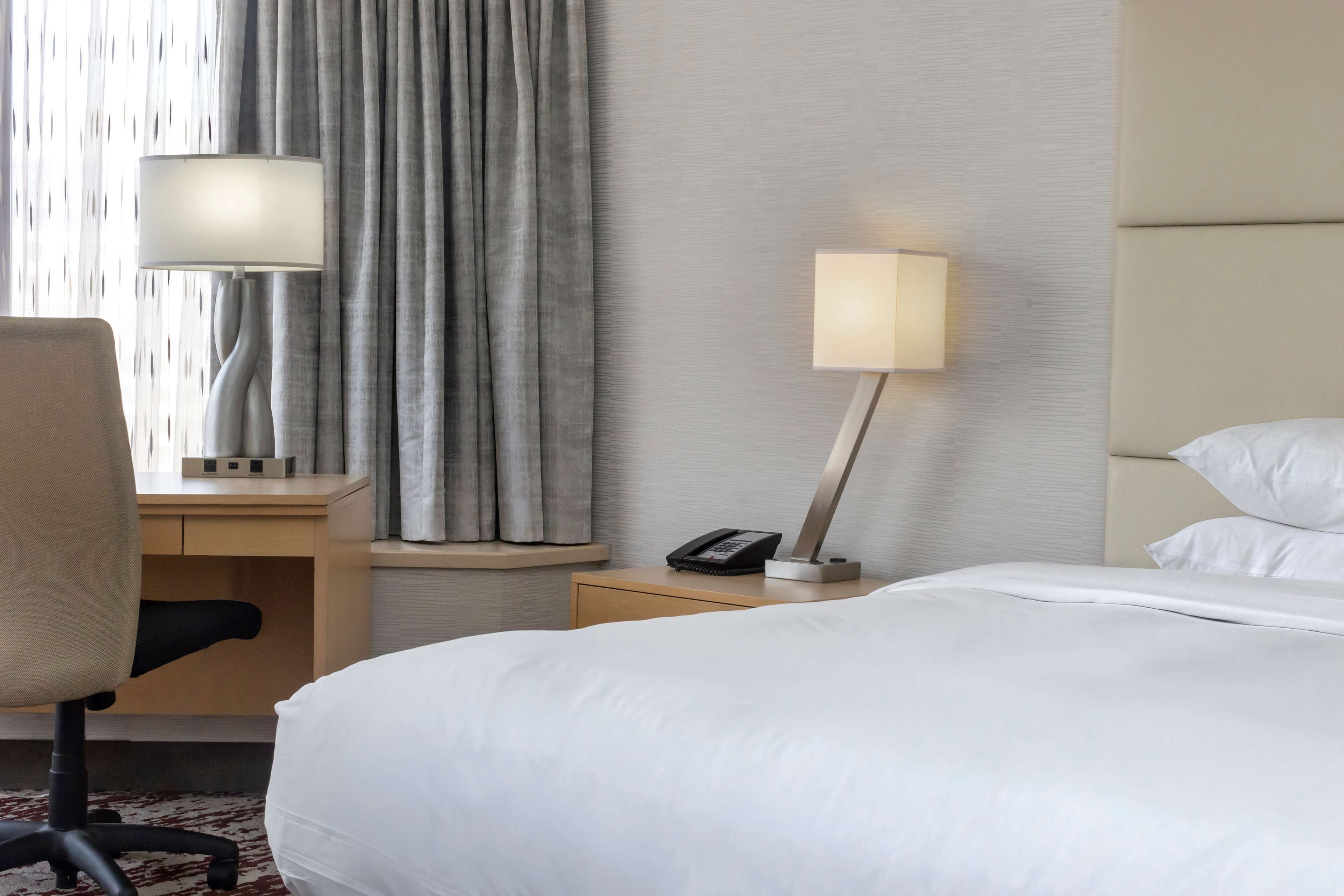A hotel room with a bed, a desk with a chair, a lamp, and a telephone.