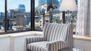 Une chambre moderne dotée d’une grande fenêtre donnant sur la ville, d’un fauteuil à rayures et d’un lampadaire.
