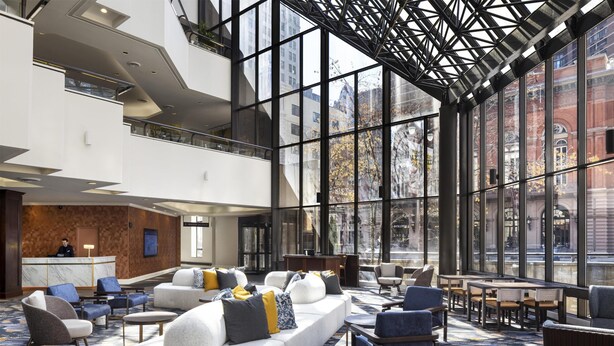 Un hall d’hôtel moderne, doté d’un plafond haut, de grandes fenêtres et d’un espace détente avec des canapés et des fauteuils.