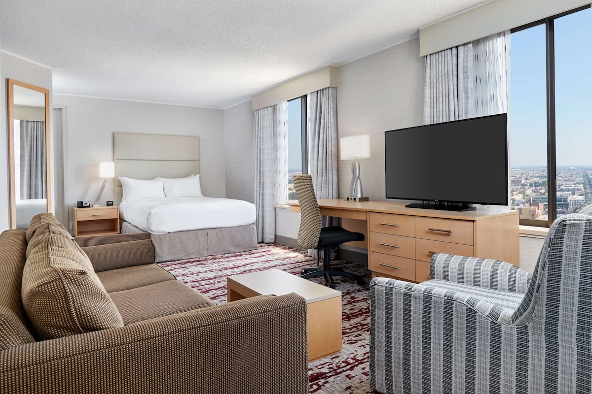 A hotel room with a bed, a desk, a television, and seating areas.
