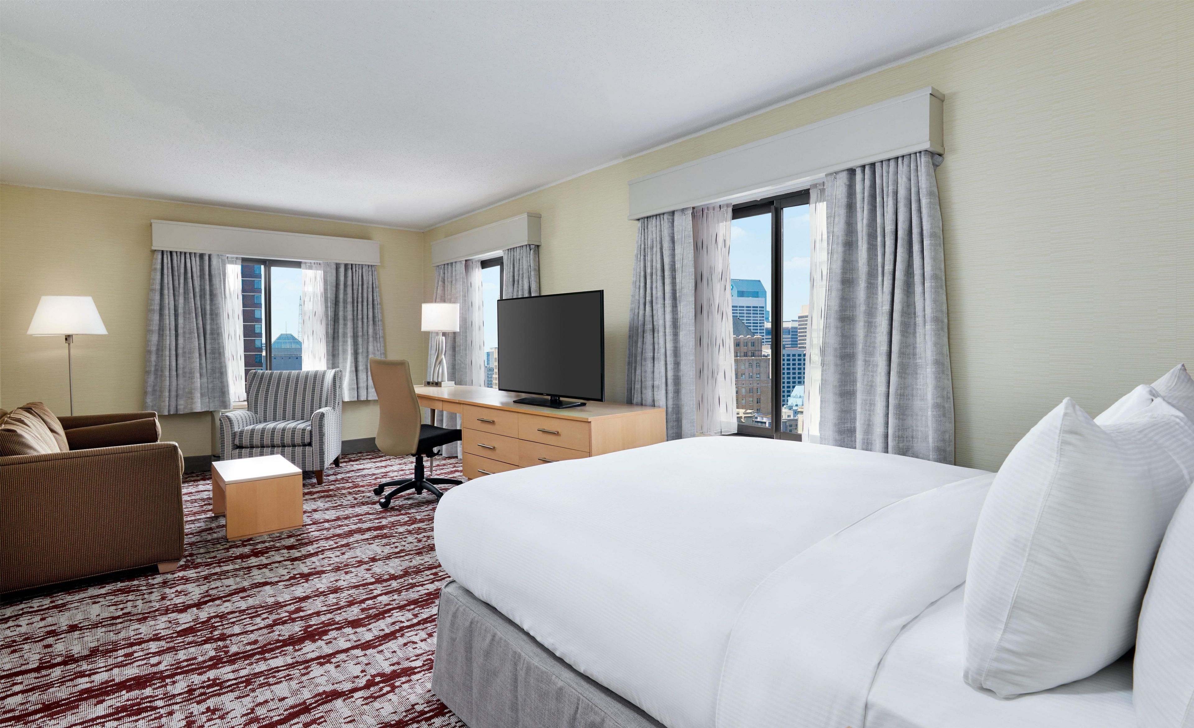 A hotel room with a bed, a desk, a chair, a TV, and a view of the city.