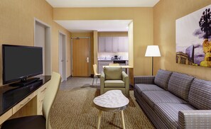 A hotel room with a flat-screen TV, a sofa, a small table, a chair, a lamp, and a painting on the wall. - DoubleTree by Hilton Philadelphia Center City (Philadelphia)