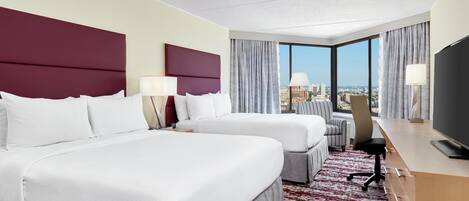 A hotel room with two beds, a desk, a chair, and a television.