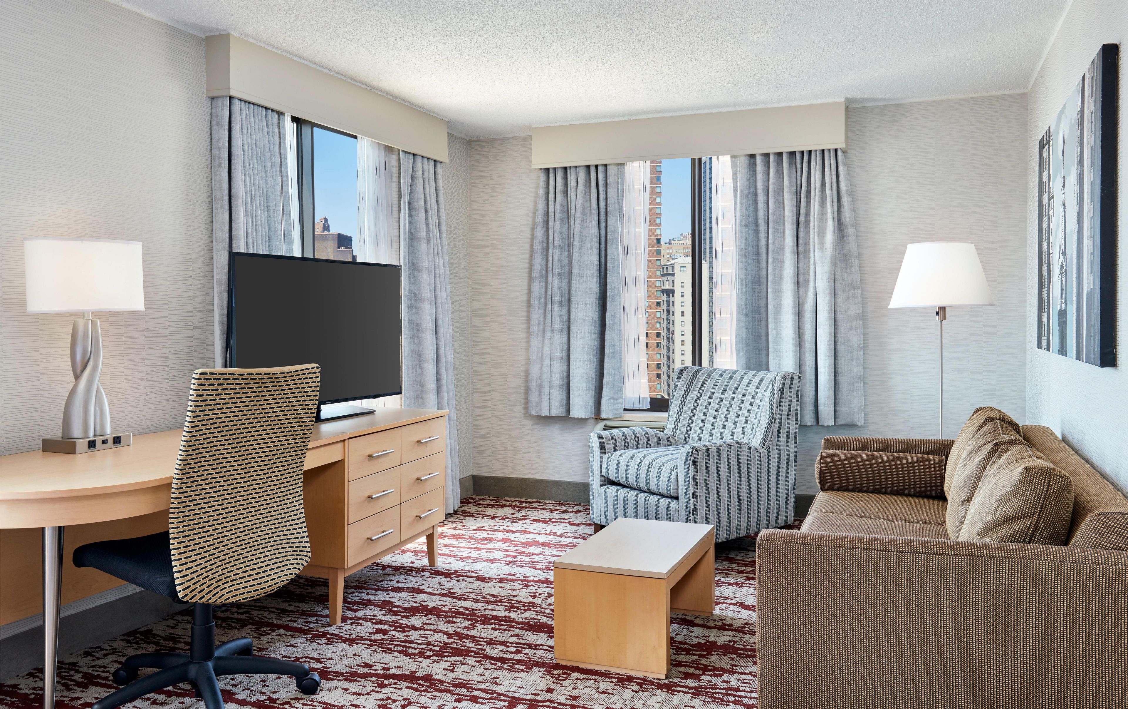 A hotel room with a desk, chair, sofa, and a TV.