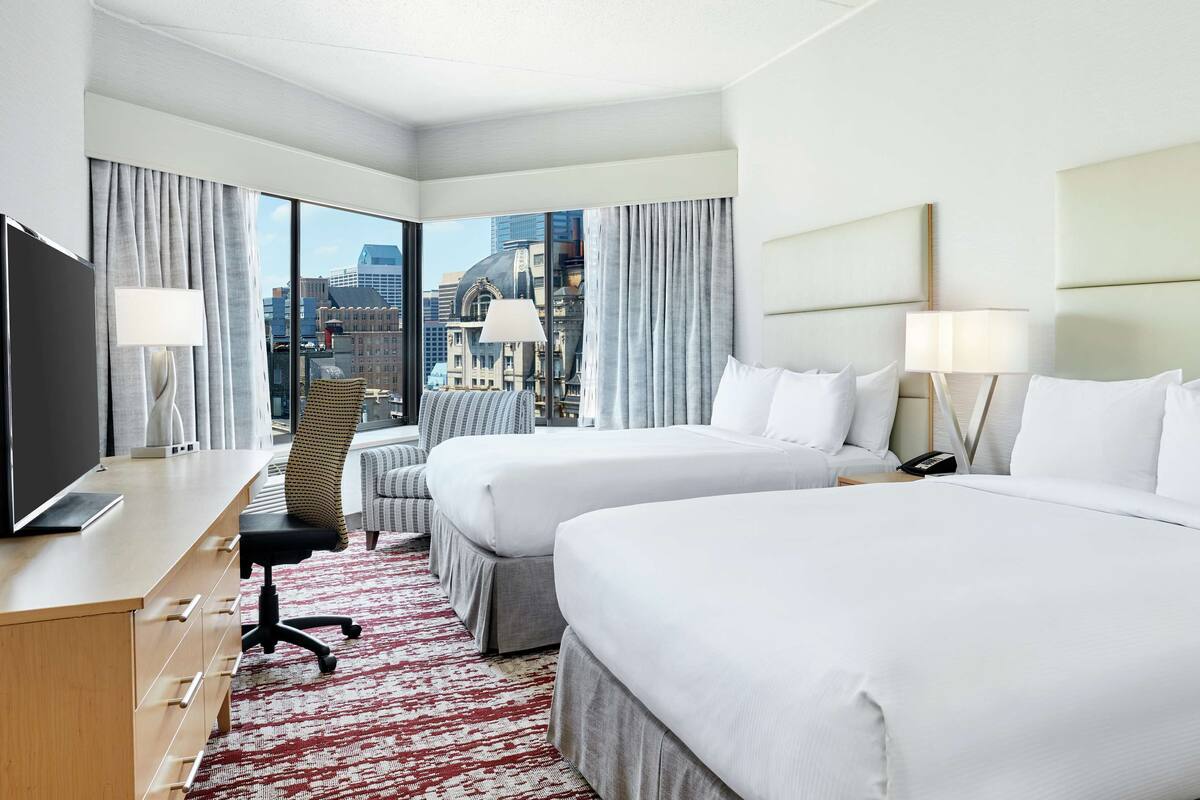 A hotel room with two beds, a desk, a chair, and a TV.