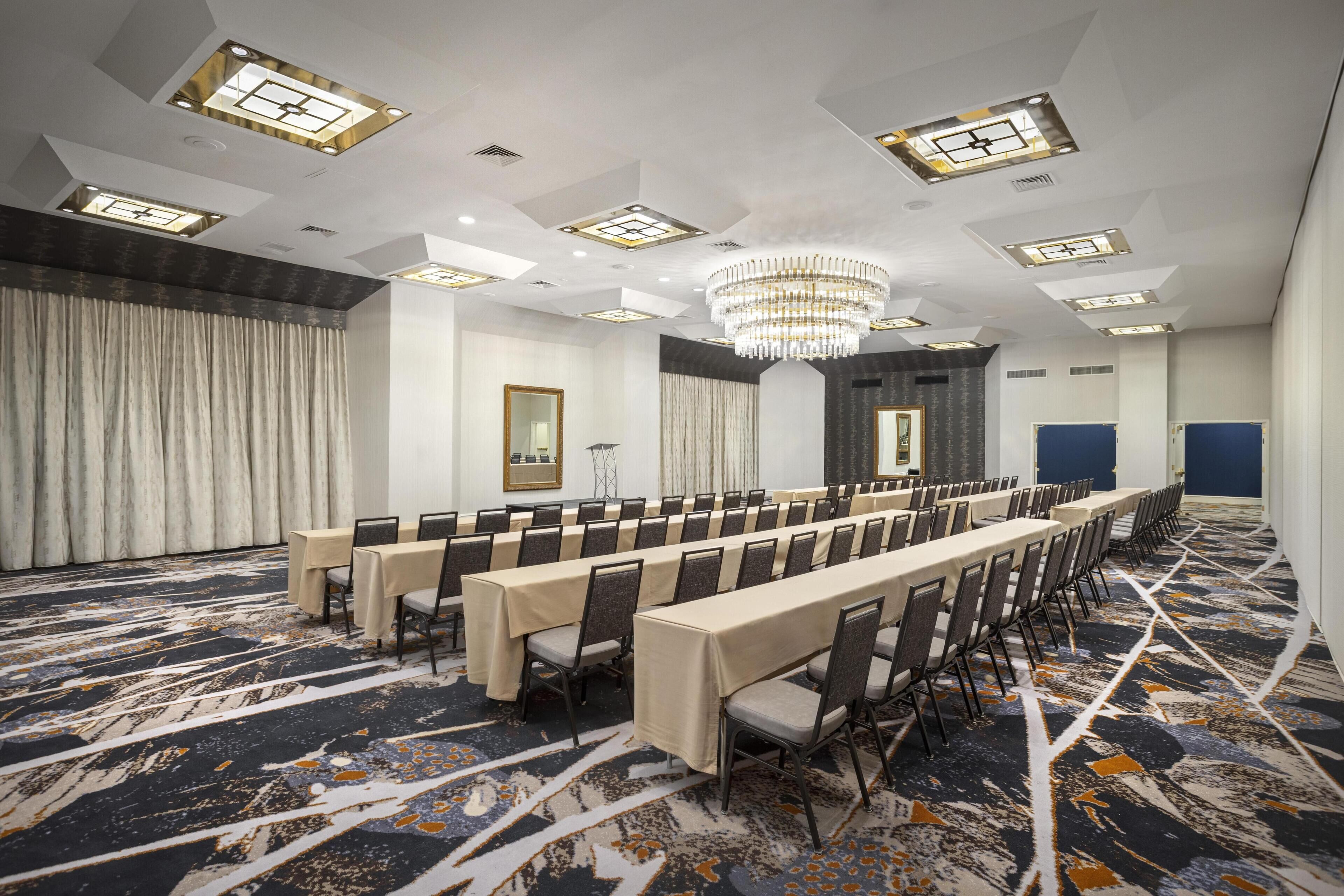 A conference room with long tables, chairs, a chandelier, and patterned carpet.