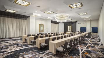 A conference room with long tables, chairs, a chandelier, and patterned carpet.