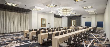 A conference room with long tables, chairs, a chandelier, and patterned carpet.