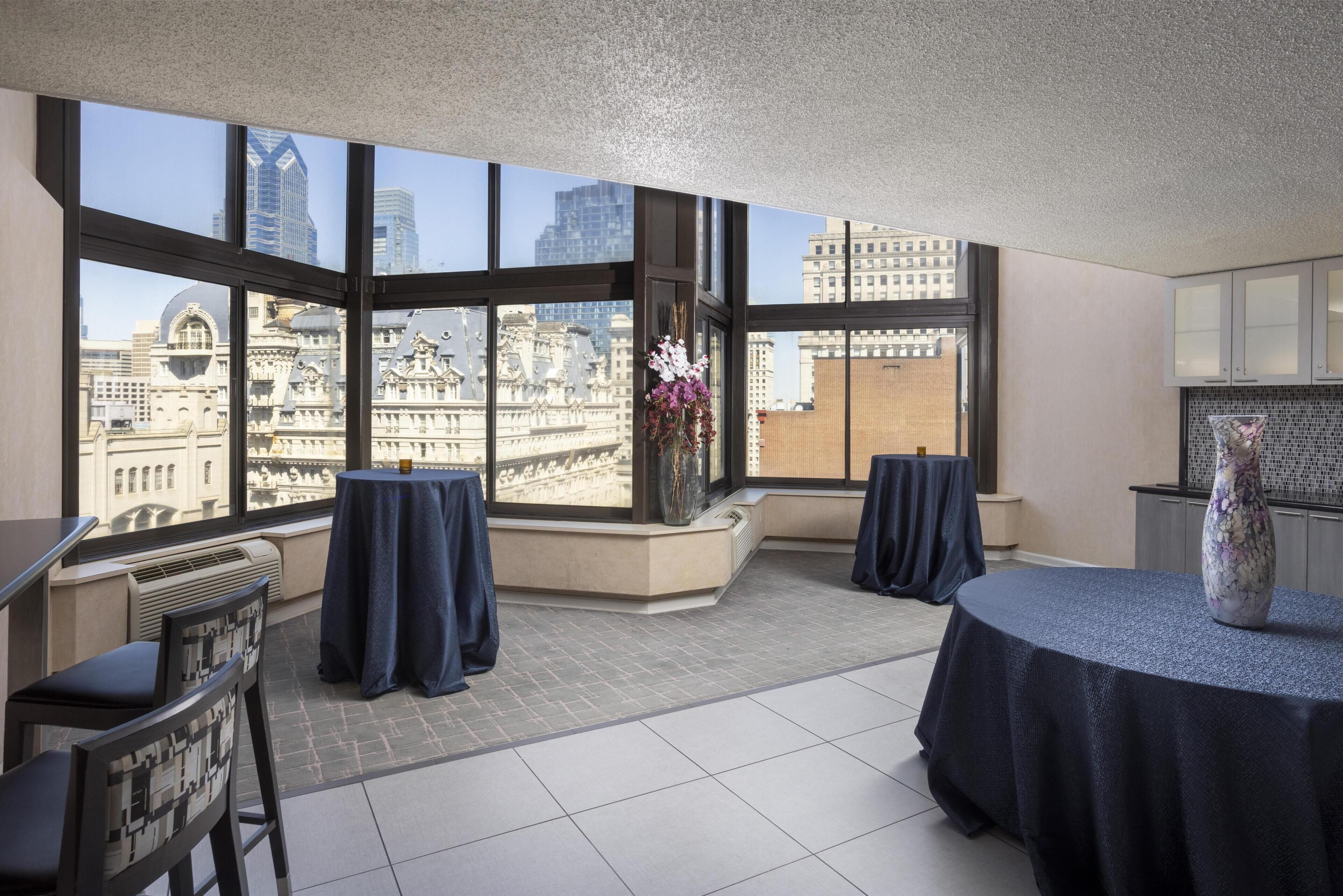 A spacious balcony with large windows offering a city view, a round table with a vase, and a chair.
