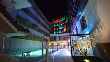 Un hotel moderno con fachada curva, piscina exterior y una escalera que lleva a un nivel superior.