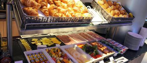 Un buffet proposant une variété de plats, notamment des pâtisseries, des fruits et des condiments.