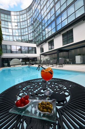 A poolside table with a drink, olives, and tomatoes, surrounded by lounge chairs and a modern building with large windows. - Holiday Inn Dijon by IHG (Dijon)