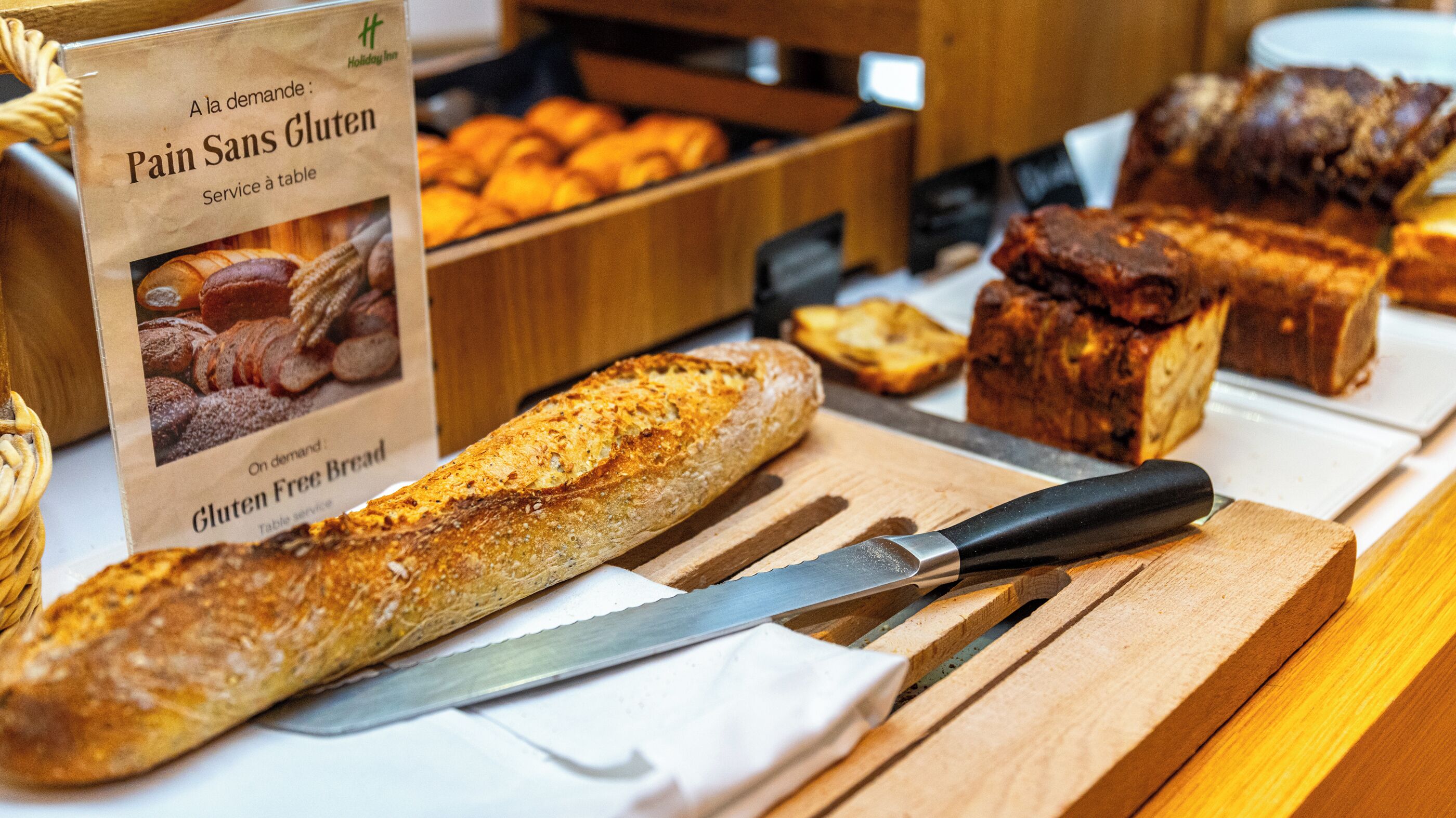 A variety of breads and pastries on a wooden table, including a sign for gluten-free options.