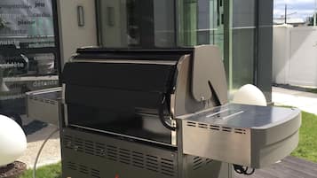 A barbecue grill with 'Barbecue Party' branding, located outdoors on a patio with a modern building in the background.