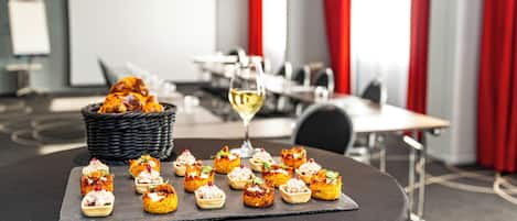 A dining table with a variety of appetizers and a glass of white wine, set in a modern dining area with red curtains and a basket of bread.