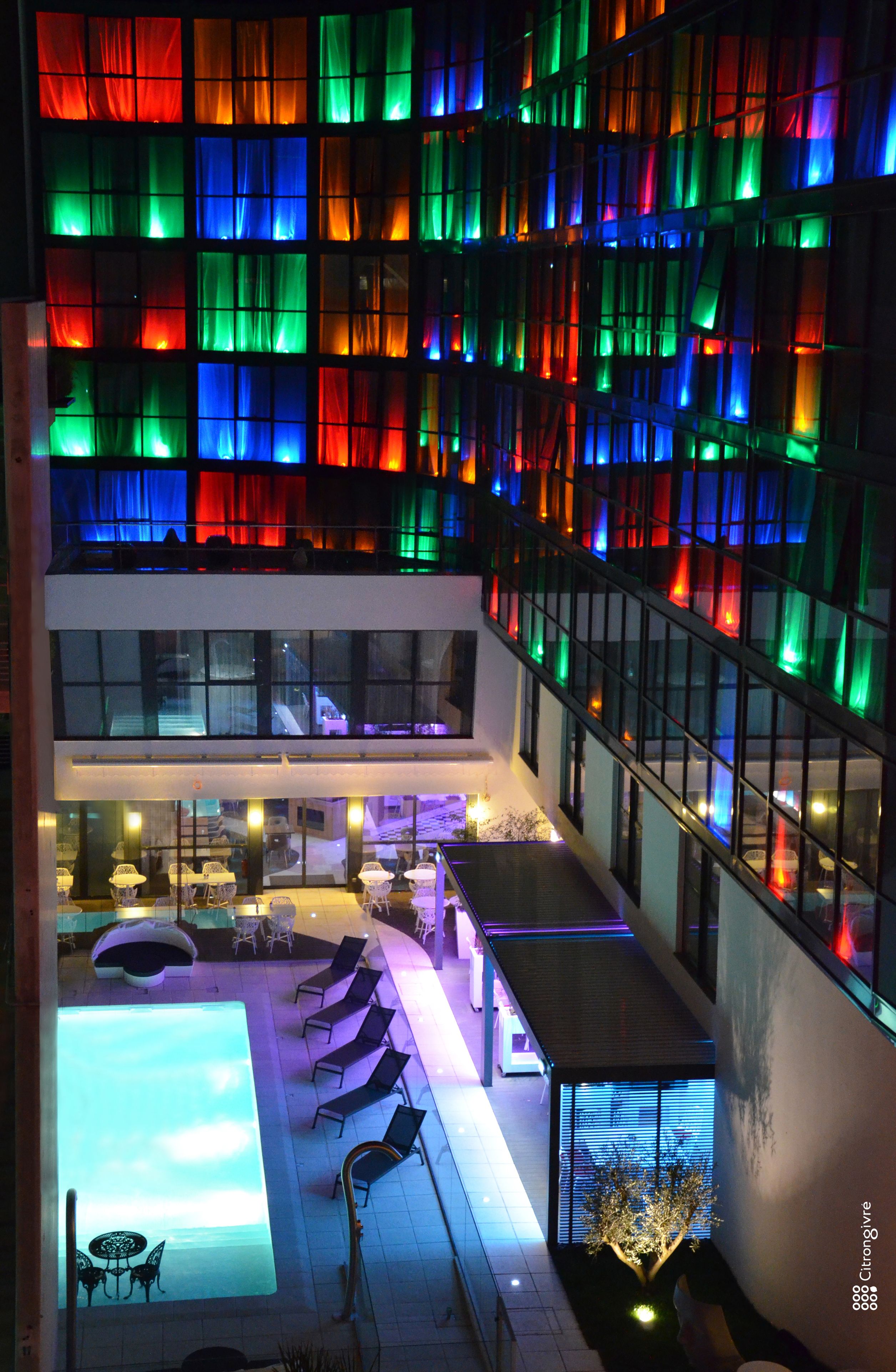 Un hôtel moderne doté d’une piscine sur le toit, d’un espace extérieur aménagé et d’une façade aux couleurs vives.
