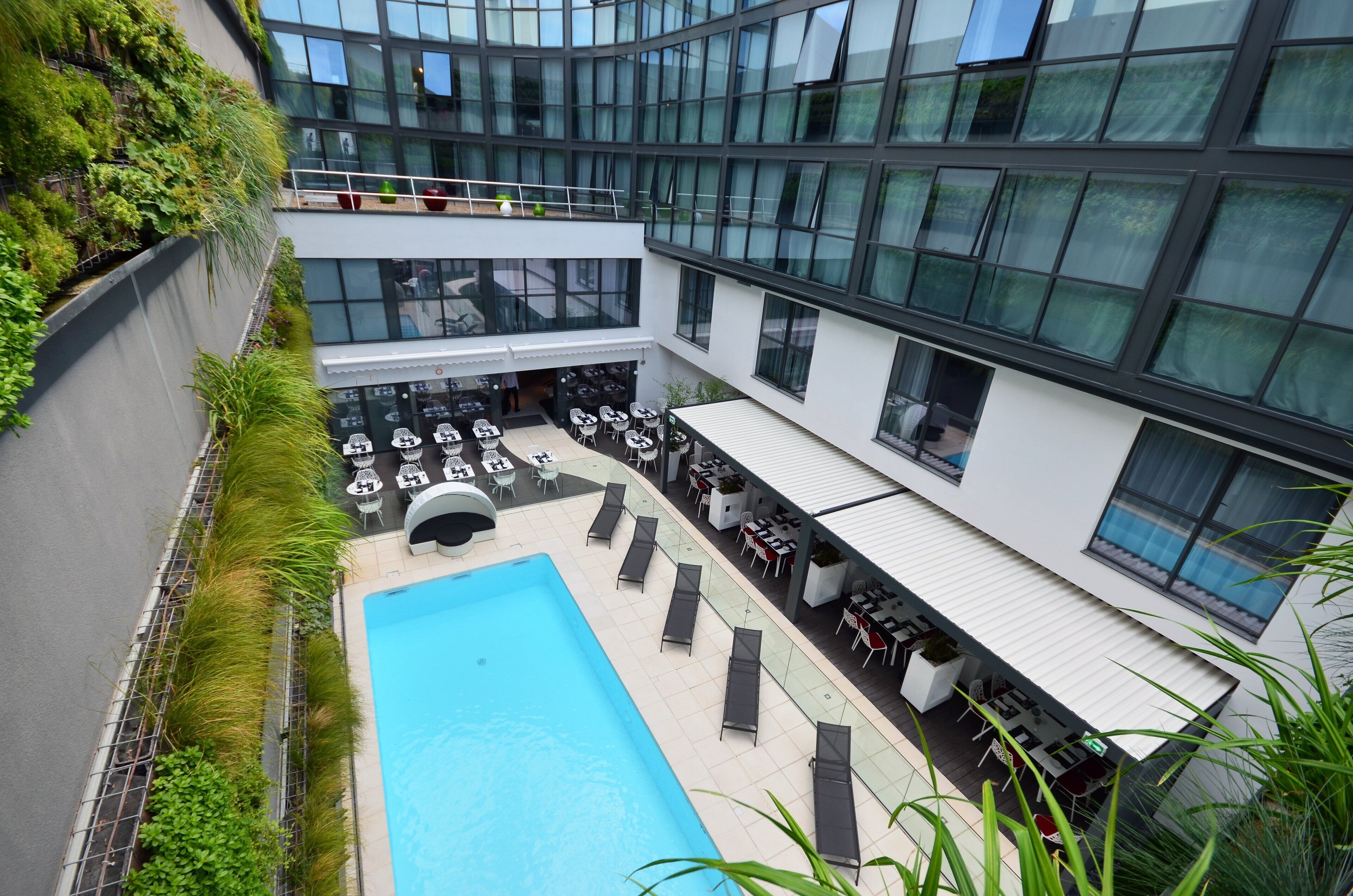 A modern building with a rooftop pool, outdoor seating, and a green wall.