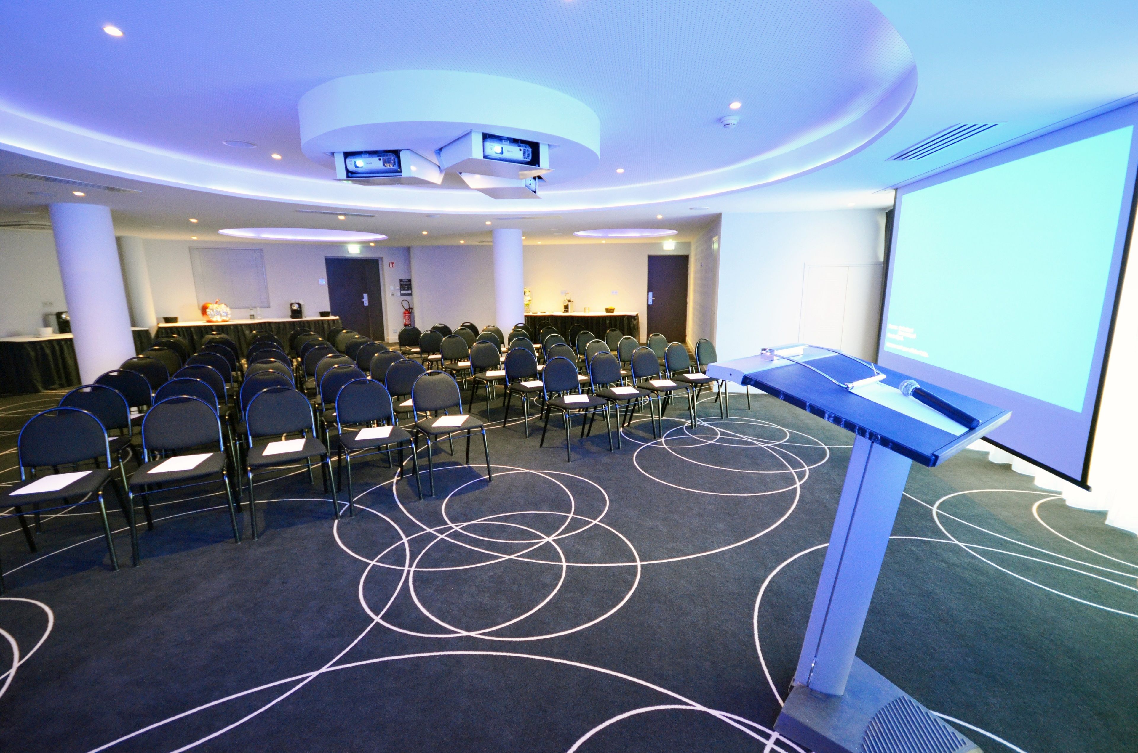 A conference room with rows of chairs, a podium, and a large screen.