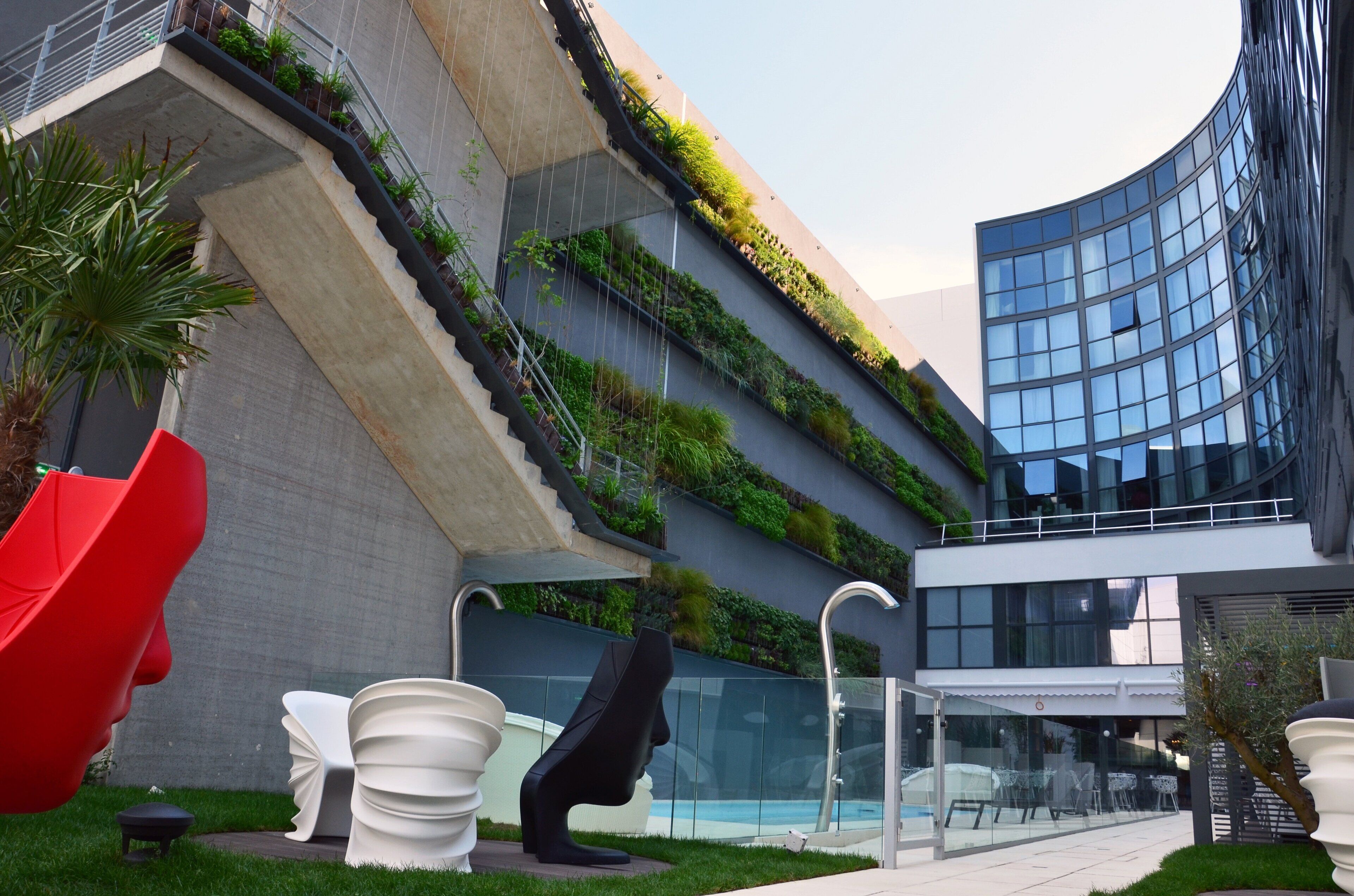 A modern building with a curved glass facade, vertical gardens, and outdoor seating areas with unique sculptural chairs.