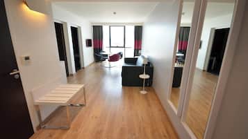 Ein modernes Hotelzimmer mit Holzboden, einer Sitzecke mit Sofa und Sesseln, einem kleinen Tisch und einem an der Wand befestigten Fernseher.
