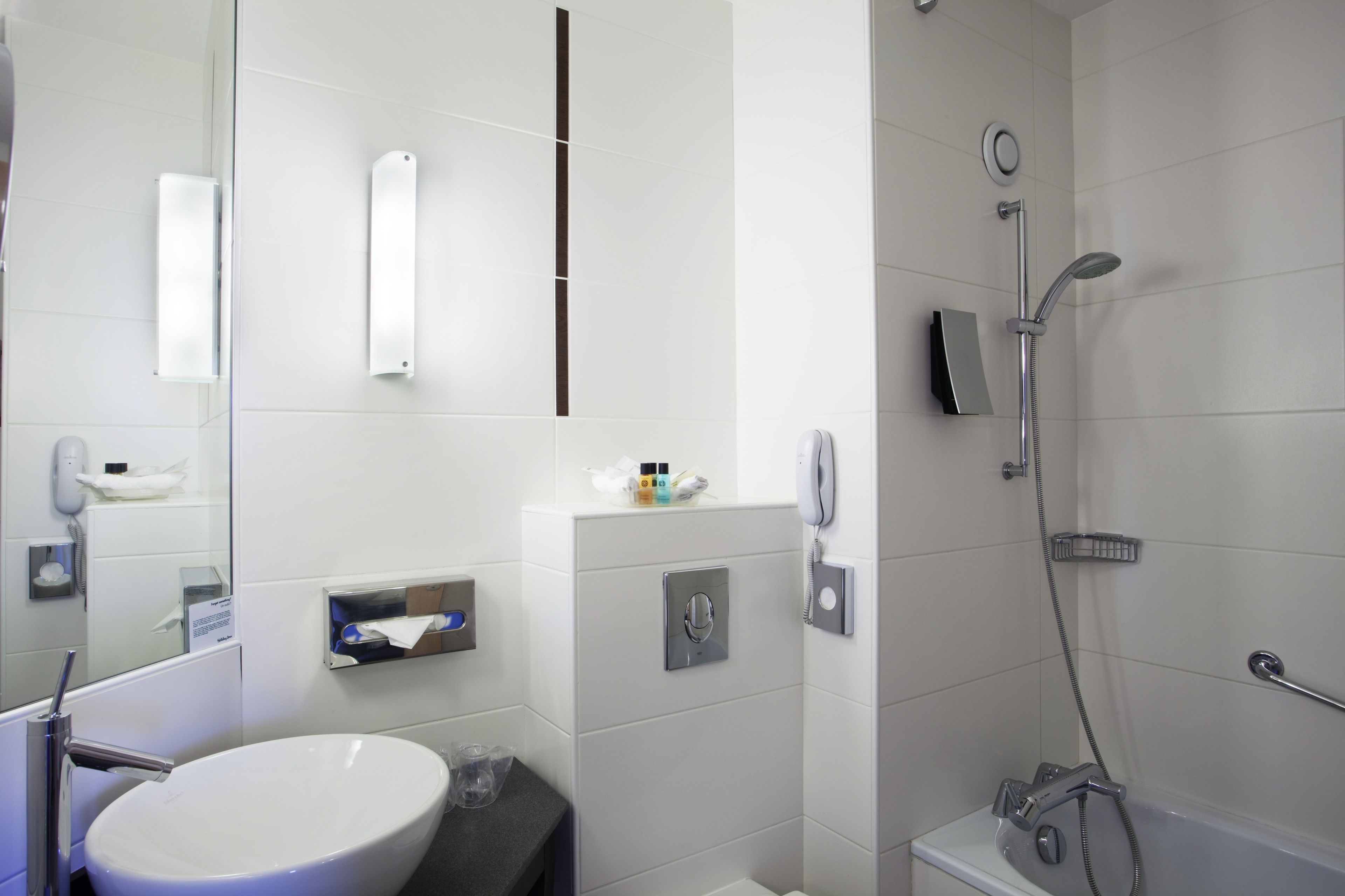 Un baño moderno con lavamanos blanco, espejo, inodoro y zona de ducha.