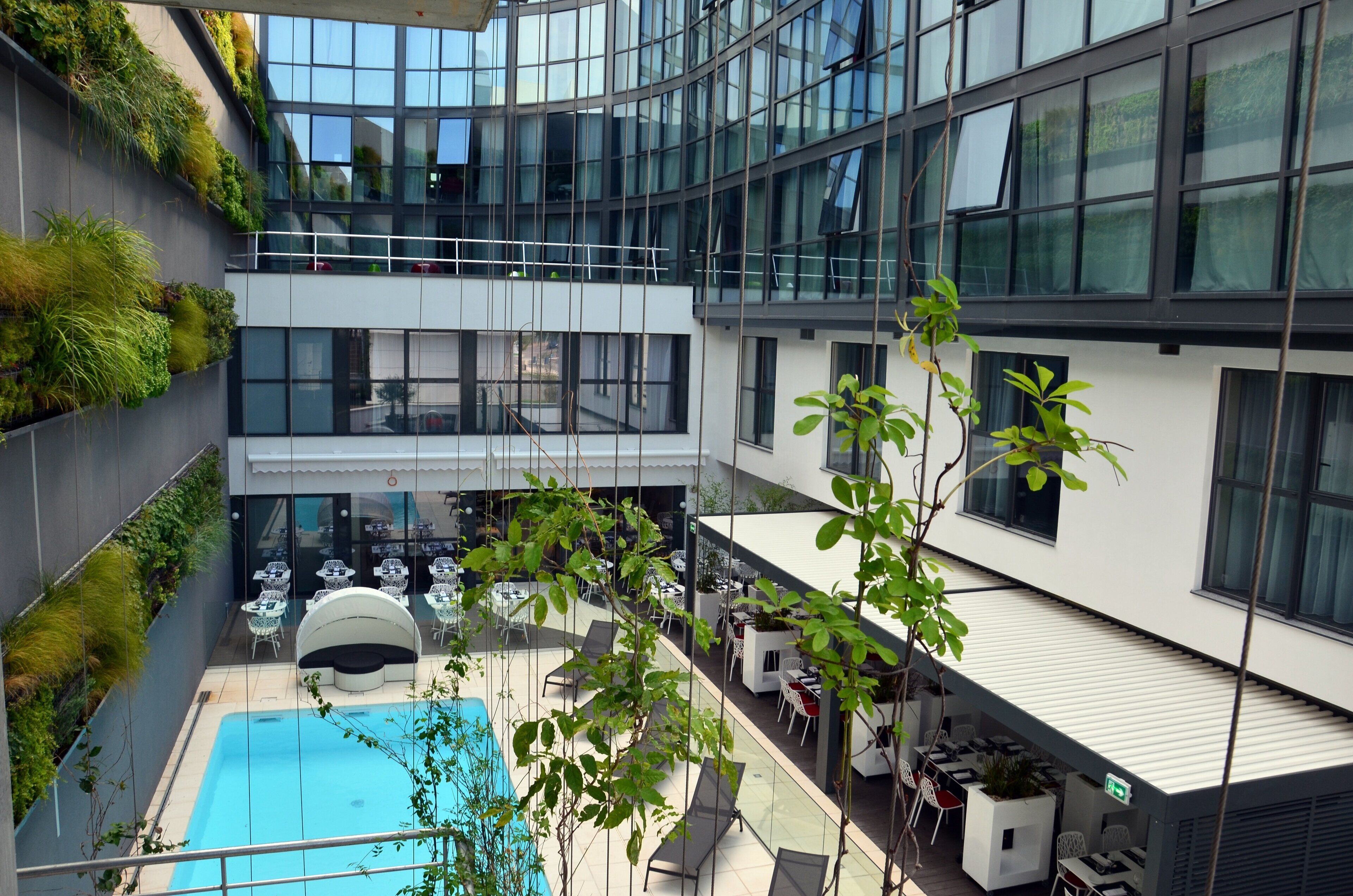 A modern building with a rooftop pool, outdoor seating, and greenery.