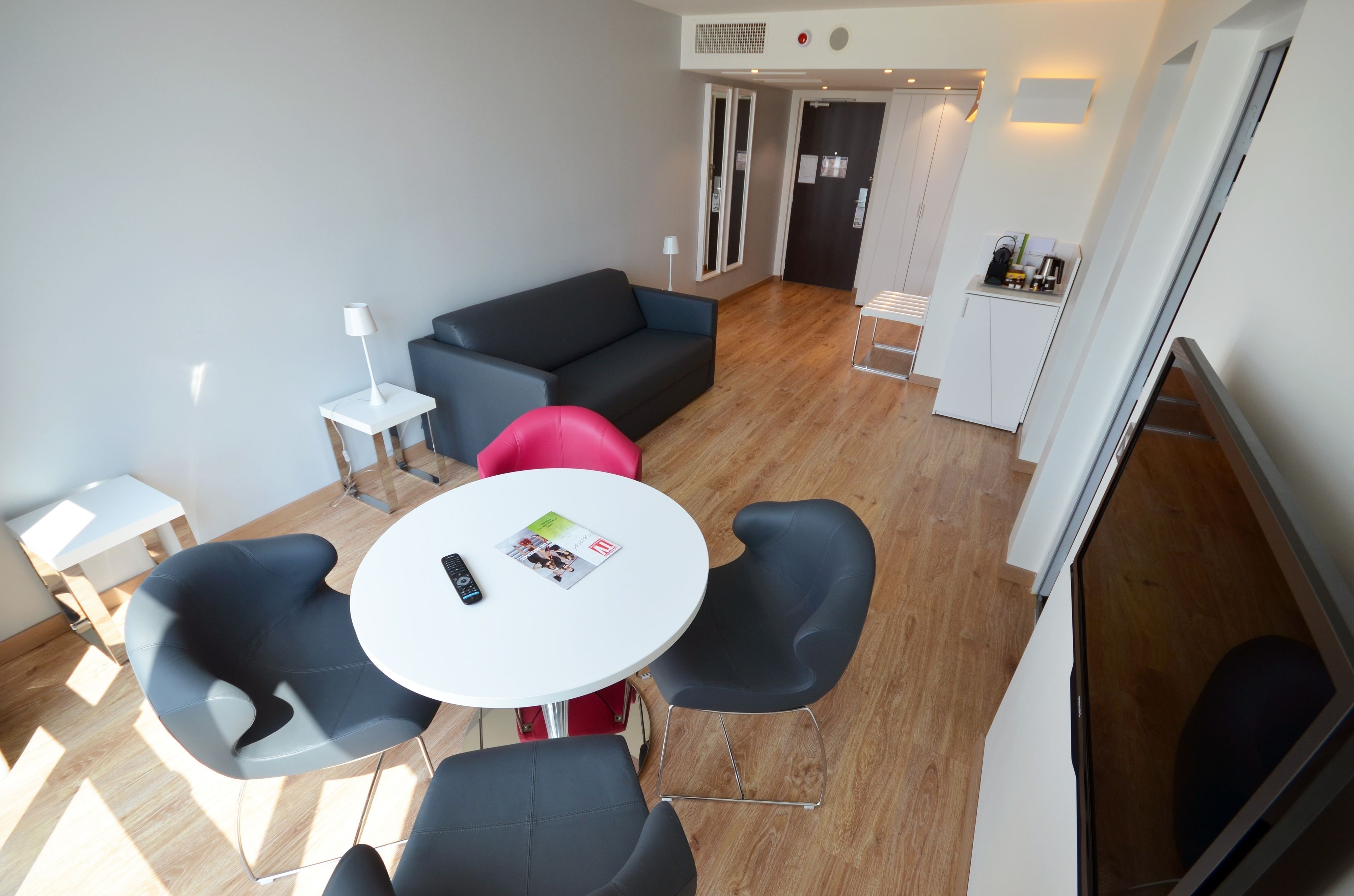 Un salon moderne avec une table ronde, des chaises noires et rouges, un canapé gris et une lampe blanche.