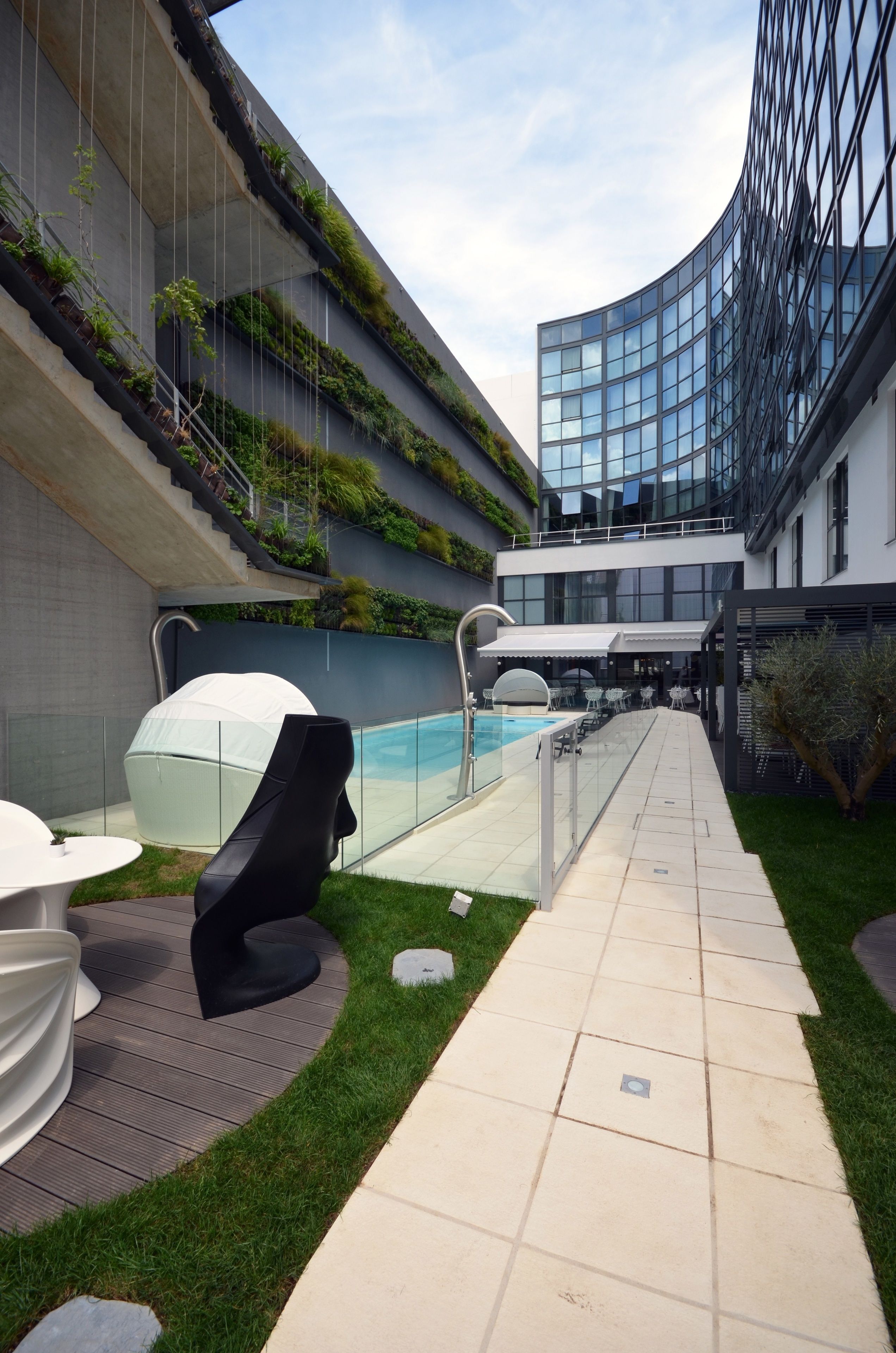 Un espacio exterior moderno con piscina, sillas de descanso y una terraza con paredes de vidrio.