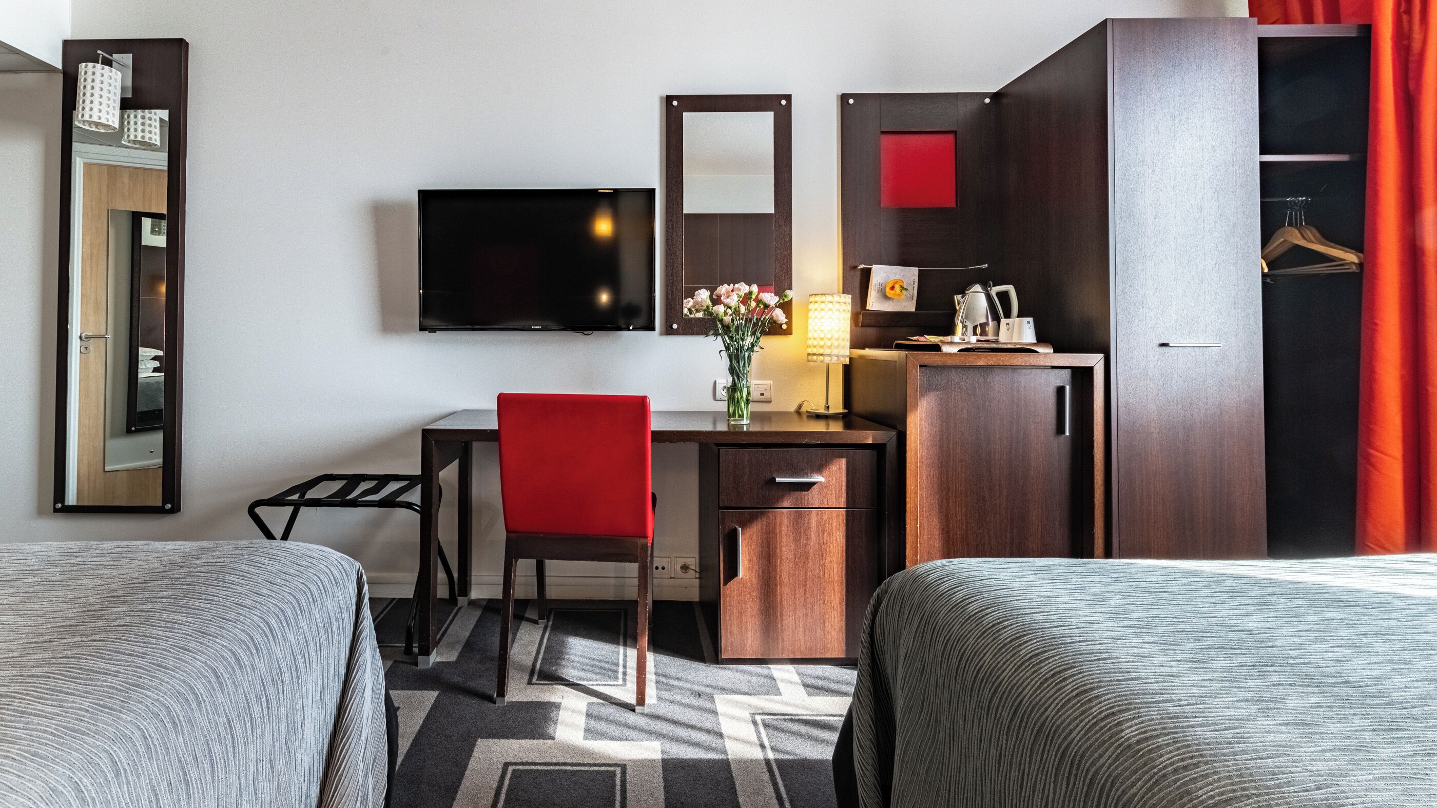 Habitació d'hotel amb dos llits, una taula de treball amb cadira, televisió, armari i mirall.