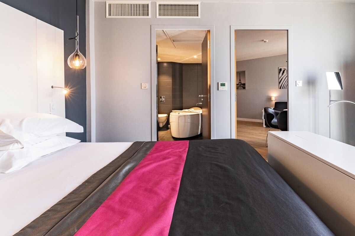 Een moderne hotelkamer met een groot bed, een bureau en een zichtbare badkamer door een geopende deur.