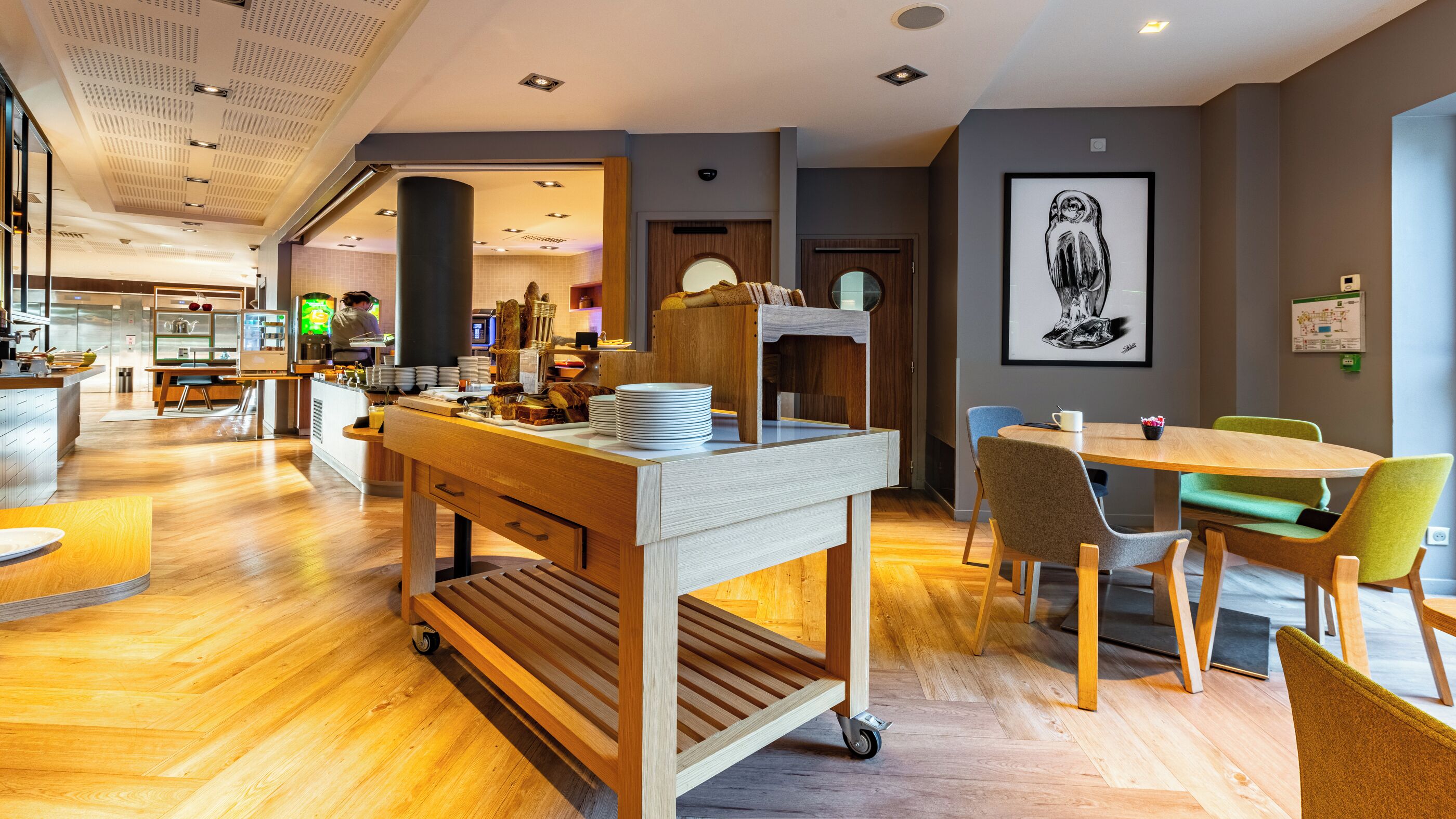 A modern dining area with a wooden table and chairs, a buffet cart with food items, and a large framed artwork on the wall.