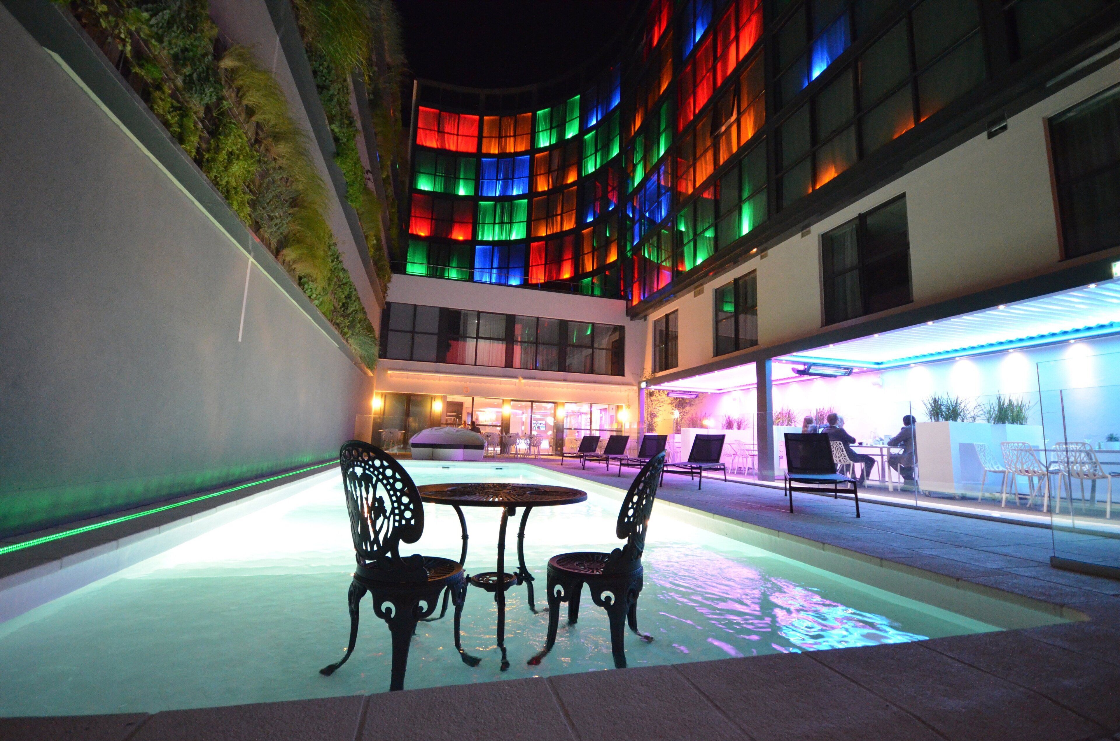 An outdoor patio area with a pool, seating, and a building with colorful lighting.