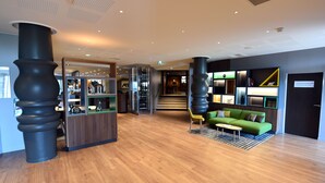 Un hall d’hôtel moderne avec un plancher en bois, un canapé vert et un comptoir d’accueil.