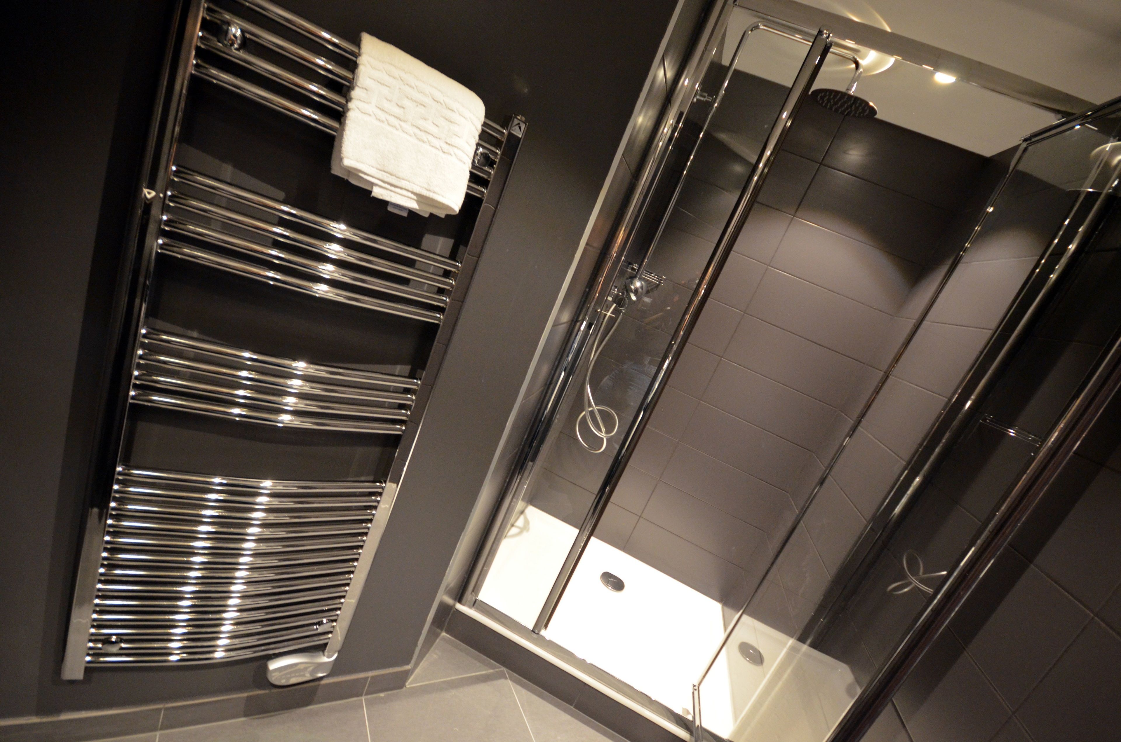 A modern bathroom with a glass shower enclosure, a chrome towel rack, and a white towel hanging on it.