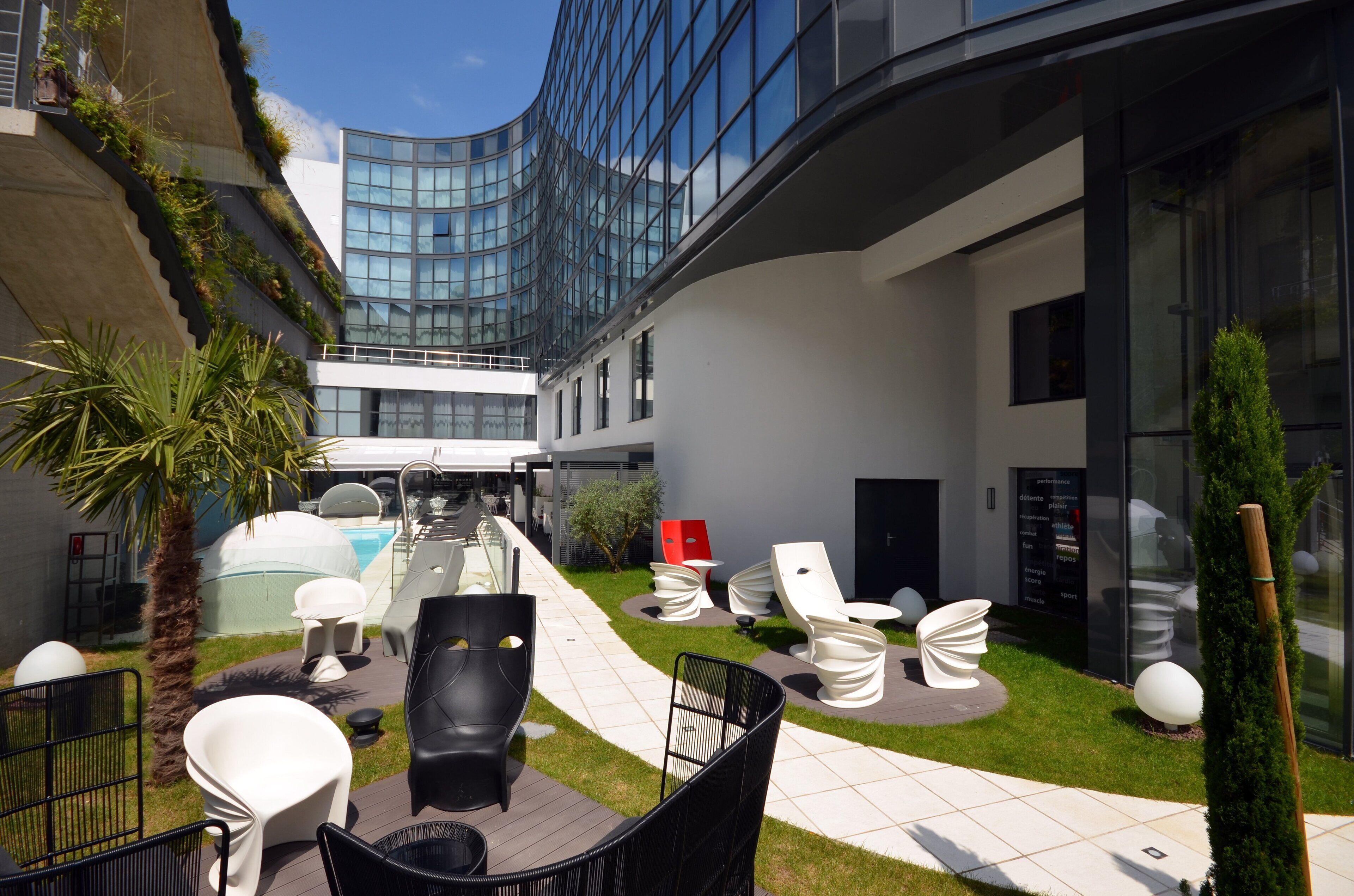 A modern outdoor lounge area with seating, a pool, and a glass building in the background.