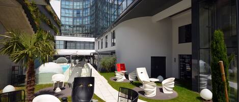 A modern outdoor lounge area with seating, a pool, and a glass building in the background.