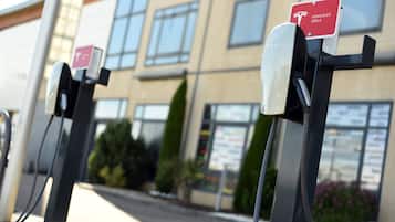 Bornes de recharge pour véhicules électriques, portant le logo Tesla, devant un bâtiment doté de grandes fenêtres et d’une enseigne.