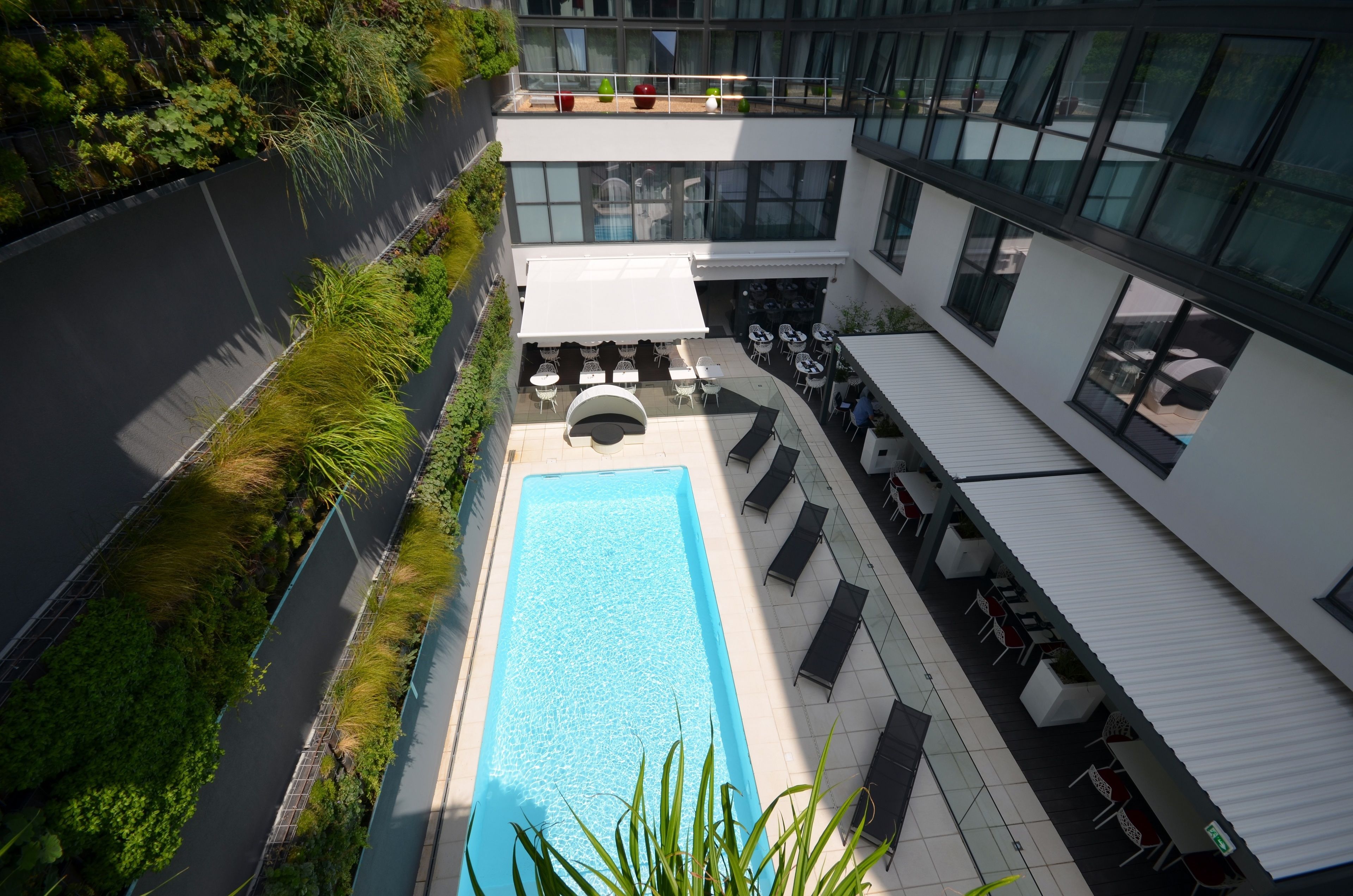 Een modern gebouw met een zwembad op het dak, terras en een groene wand.