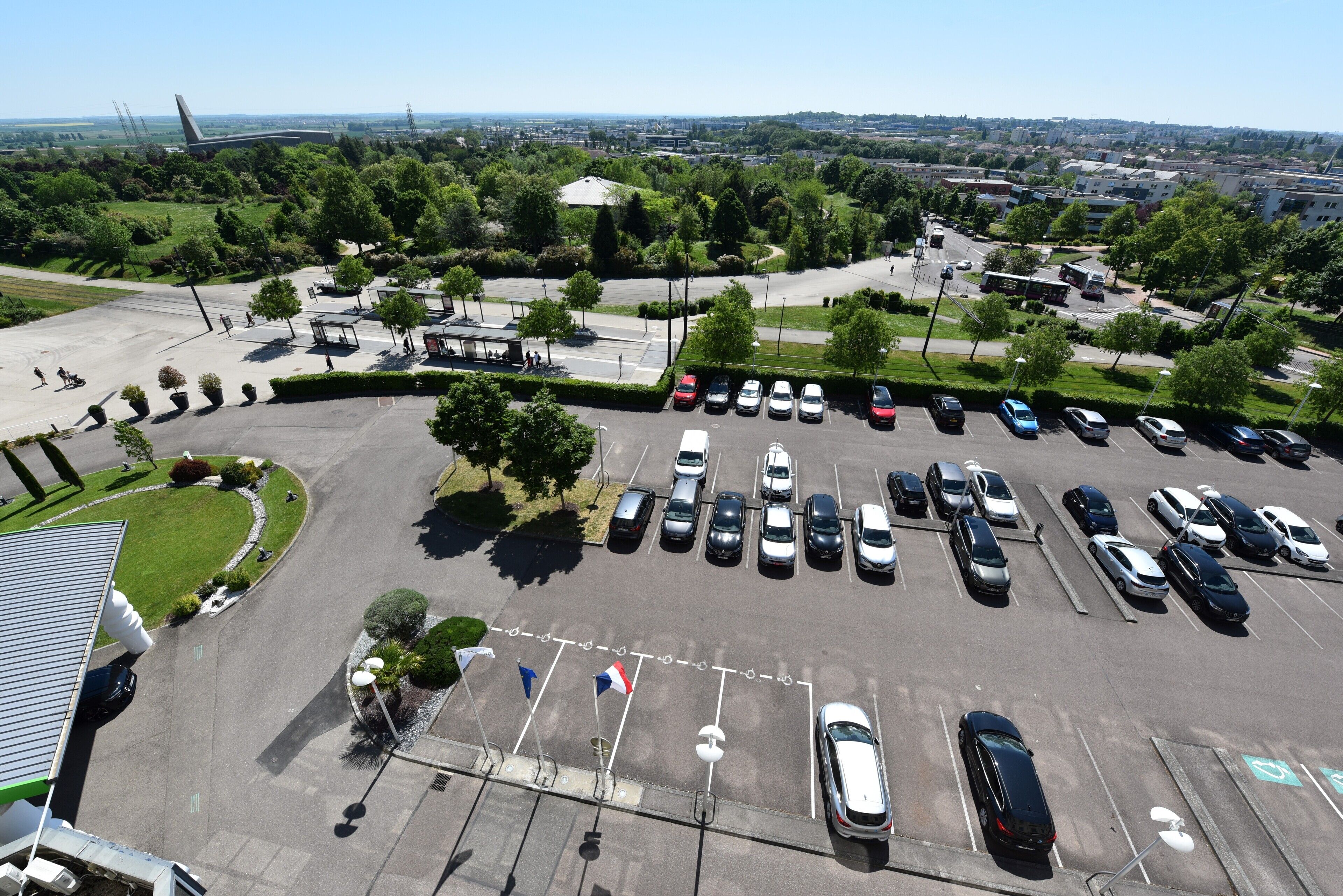 An aerial view of a parking lot with multiple cars, a few pedestrians, and surrounding greenery.