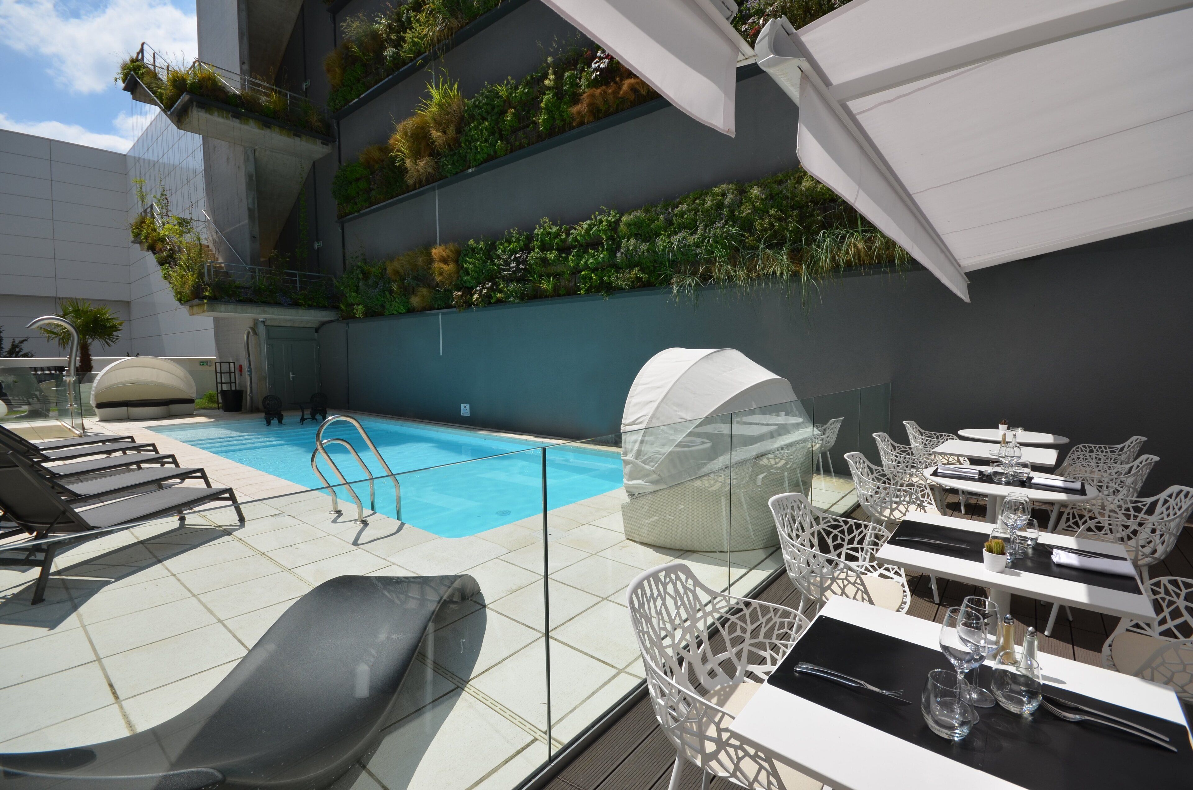 A rooftop pool area with lounge chairs, a covered seating area, and a vertical garden wall.
