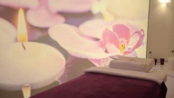 A room with a bed, a wall-mounted TV displaying flowers, and a lit candle.