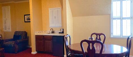 A dining area with a round table and chairs, a kitchen with a tiled backsplash, and a red patterned carpet.
